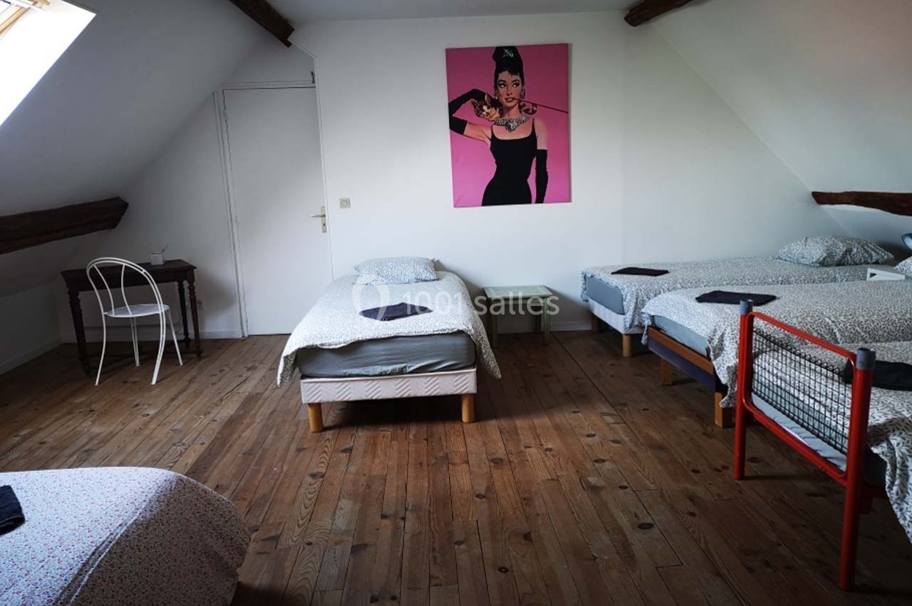 Chambre mansardée avec quatre lits simples, parquet en bois, bureau et affiche décorative sur le mur.