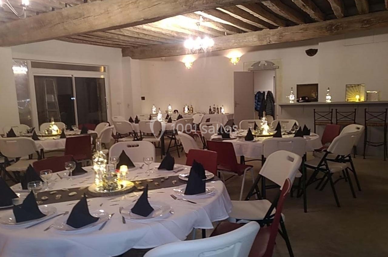 Salle décorée pour un événement avec des tables rondes dressées, nappes blanches et serviettes noires pliées.