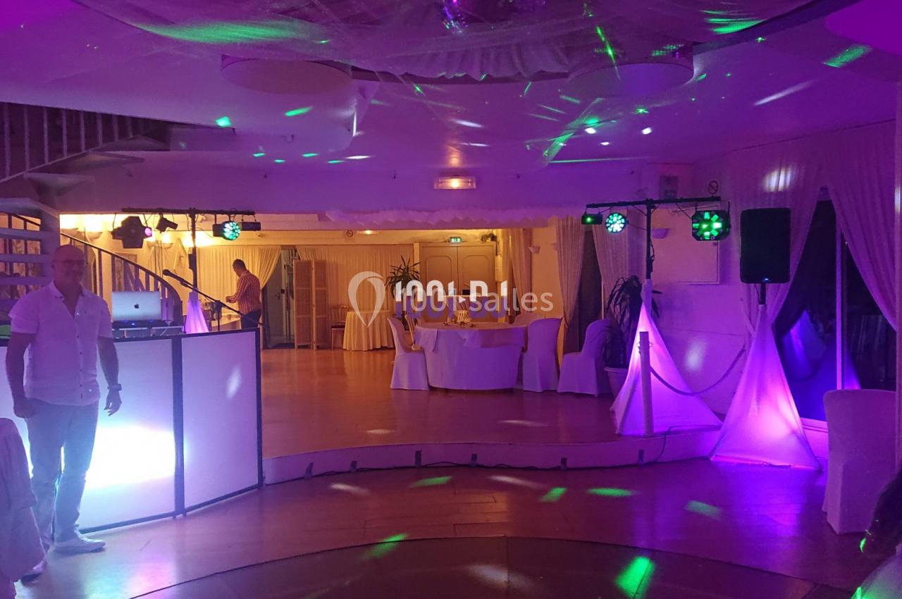 Salle de réception décorée avec éclairages colorés, piste de danse et tables dressées en arrière-plan.