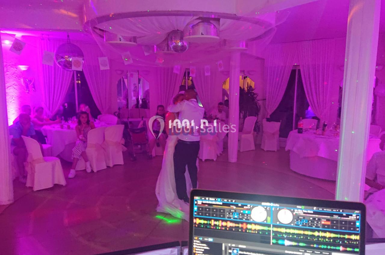 Un couple danse au centre d'une salle éclairée par des lumières colorées, entouré d'invités assis à des tables.