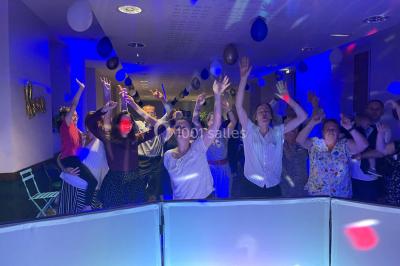 Un couple pose près d'une table décorée de fleurs et d'une pyramide de coupes de champagne dans une salle éclairée.