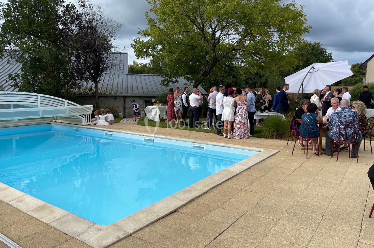 Groupe de personnes réunies près d'une piscine extérieure, avec des arbres et des tables dressées en arrière-plan.