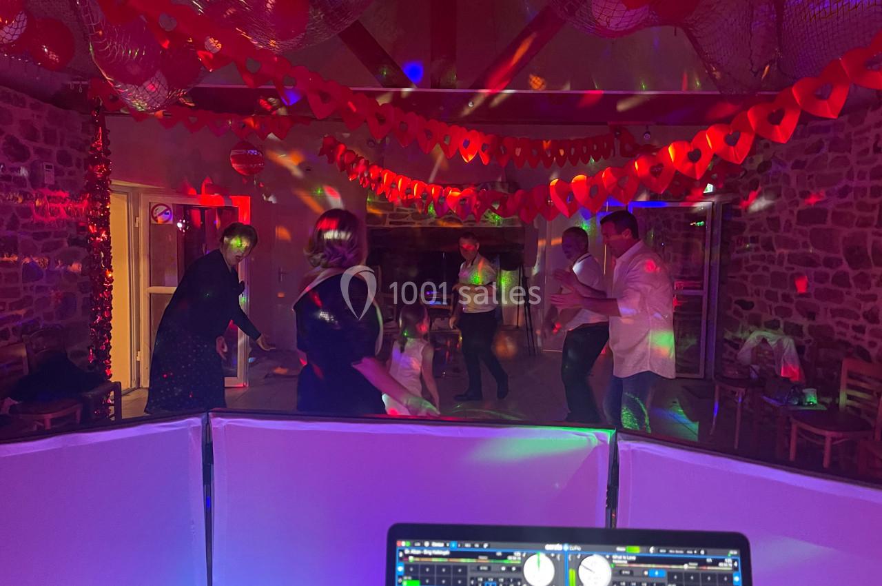 Des personnes dansent sous des lumières colorées dans une salle décorée de guirlandes rouges, vue depuis une table de DJ.