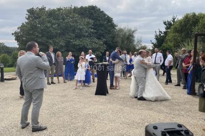 Un couple pose près d'une table décorée de fleurs et d'une pyramide de coupes de champagne dans une salle éclairée.