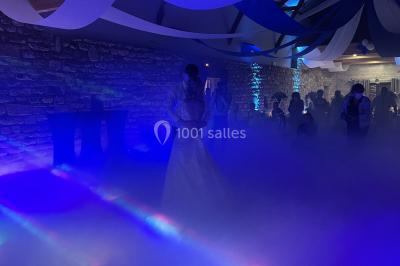 Un couple pose près d'une table décorée de fleurs et d'une pyramide de coupes de champagne dans une salle éclairée.