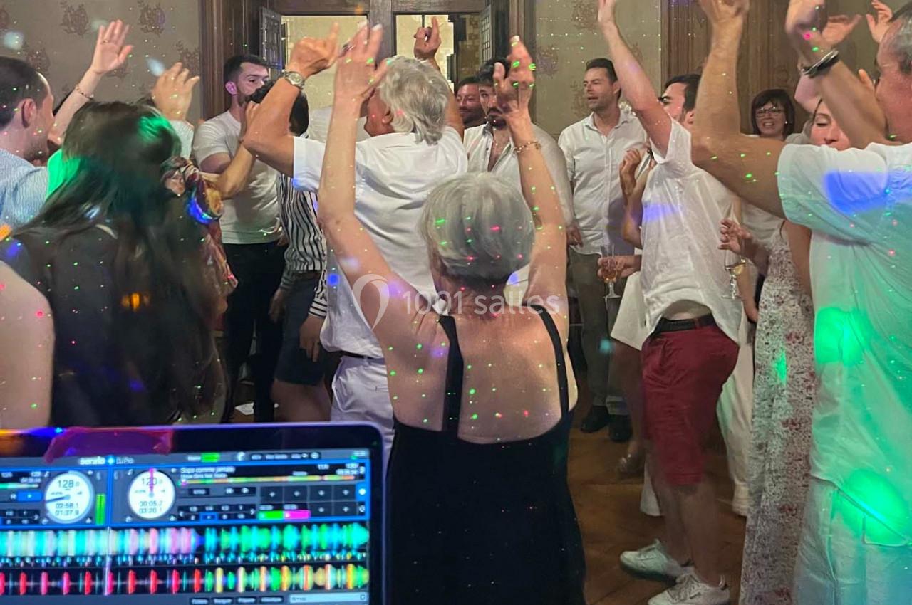 Groupe de personnes dansant dans une pièce éclairée par des lumières colorées, avec une table de mixage au premier plan.