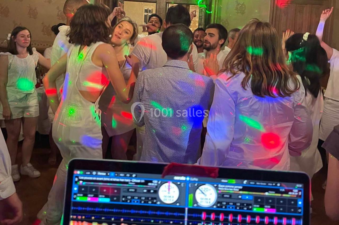Personnes dansant dans une ambiance festive avec des lumières colorées, vue depuis une table de mixage de DJ.