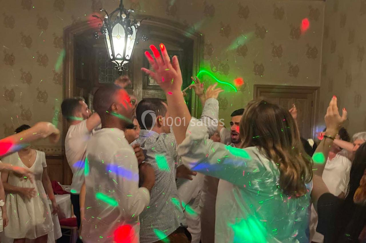 Des personnes dansent sous des lumières colorées dans une salle décorée, créant une ambiance festive.