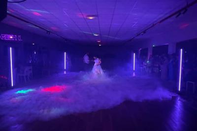 Un couple pose près d'une table décorée de fleurs et d'une pyramide de coupes de champagne dans une salle éclairée.