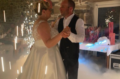 Un couple pose près d'une table décorée de fleurs et d'une pyramide de coupes de champagne dans une salle éclairée.