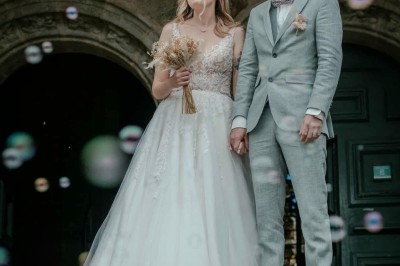 Un couple pose près d'une table décorée de fleurs et d'une pyramide de coupes de champagne dans une salle éclairée.