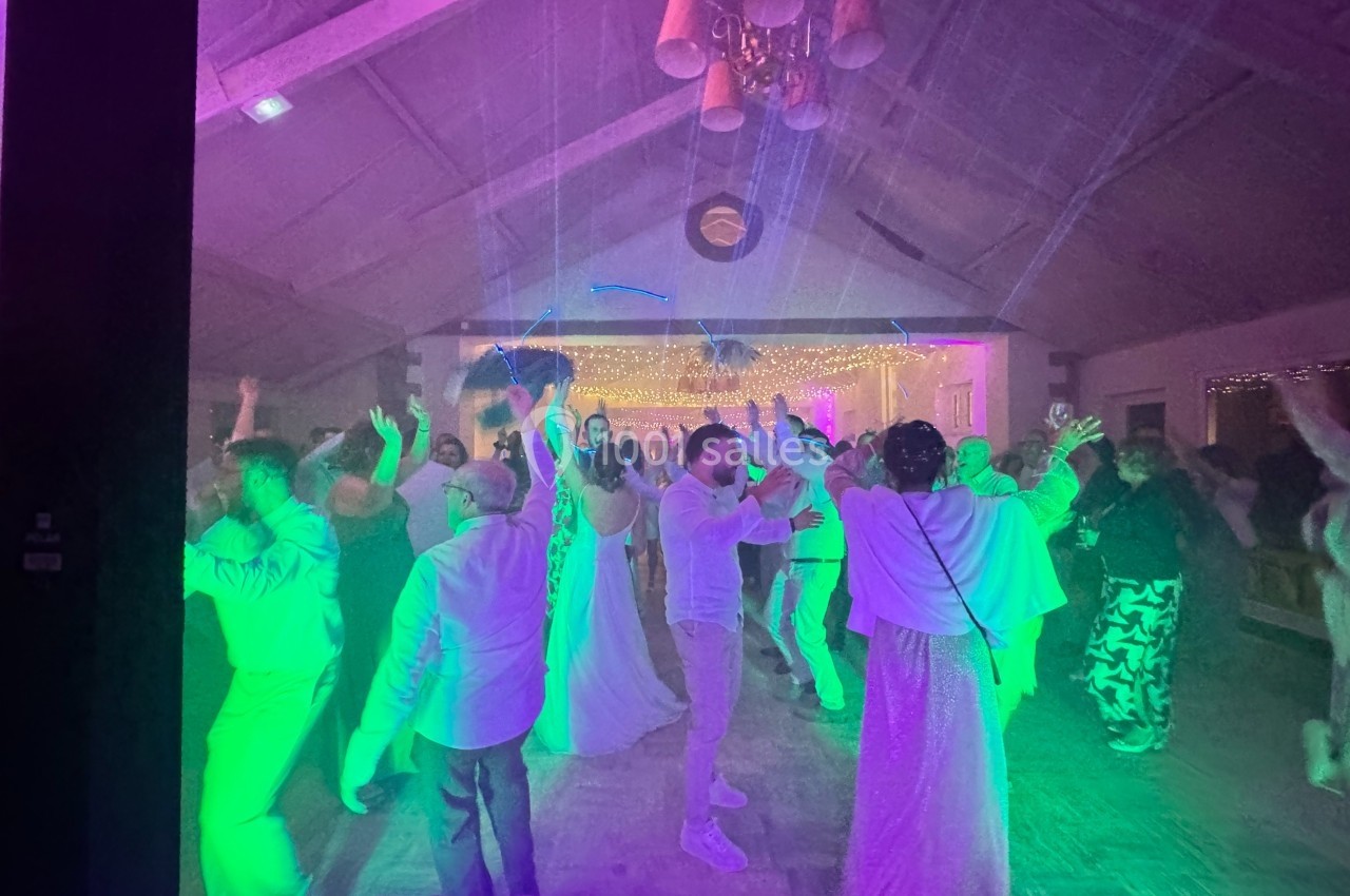 Personnes dansant sous des lumières colorées dans une salle décorée, ambiance festive et animée.