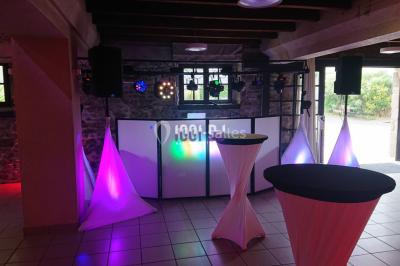 Salle en pierre avec plafond en poutres apparentes, éclairages décoratifs suspendus et équipement audio-visuel installé.