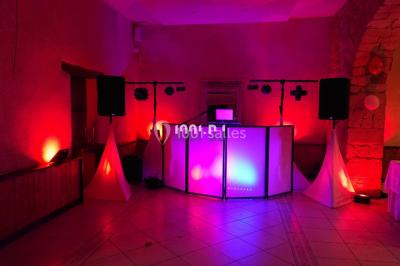 Salle en pierre avec plafond en poutres apparentes, éclairages décoratifs suspendus et équipement audio-visuel installé.