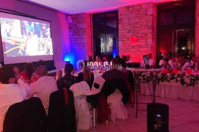 Salle en pierre avec plafond en poutres apparentes, éclairages décoratifs suspendus et équipement audio-visuel installé.