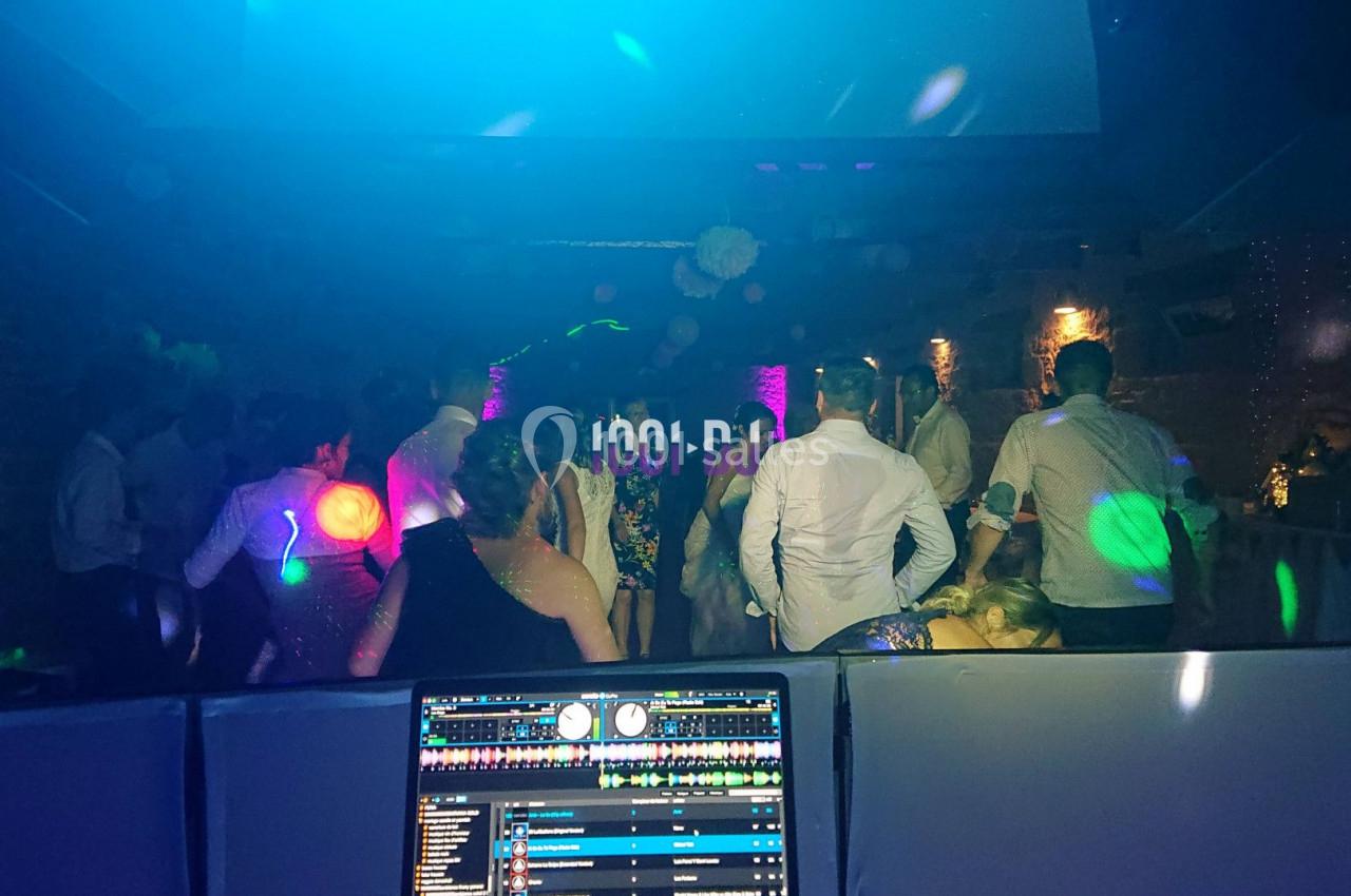 Des personnes dansent dans une salle sombre éclairée par des lumières colorées, avec une console de DJ au premier plan.