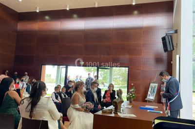 Salle en pierre avec plafond en poutres apparentes, éclairages décoratifs suspendus et équipement audio-visuel installé.