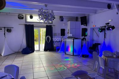 Salle en pierre avec plafond en poutres apparentes, éclairages décoratifs suspendus et équipement audio-visuel installé.