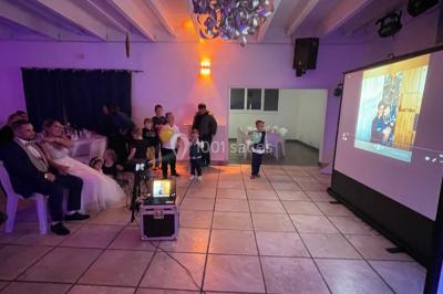 Salle en pierre avec plafond en poutres apparentes, éclairages décoratifs suspendus et équipement audio-visuel installé.