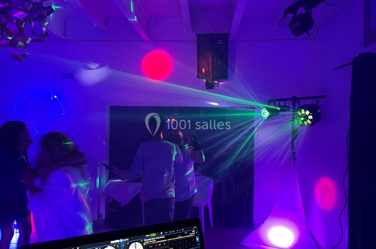 Des personnes dansent sous des lumières colorées dans une salle, avec un ordinateur affichant un logiciel de mixage au…
