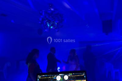 Salle en pierre avec plafond en poutres apparentes, éclairages décoratifs suspendus et équipement audio-visuel installé.