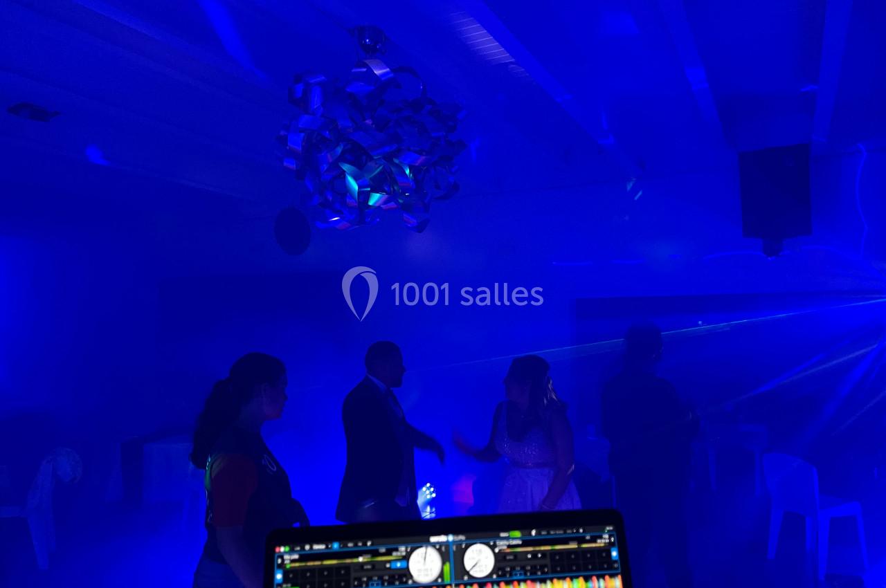 Des personnes dansent sous des lumières colorées dans une ambiance festive, avec une console DJ visible au premier plan.