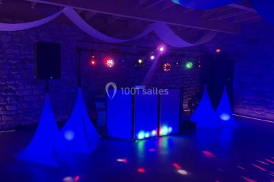 Salle en pierre avec plafond en poutres apparentes, éclairages décoratifs suspendus et équipement audio-visuel installé.