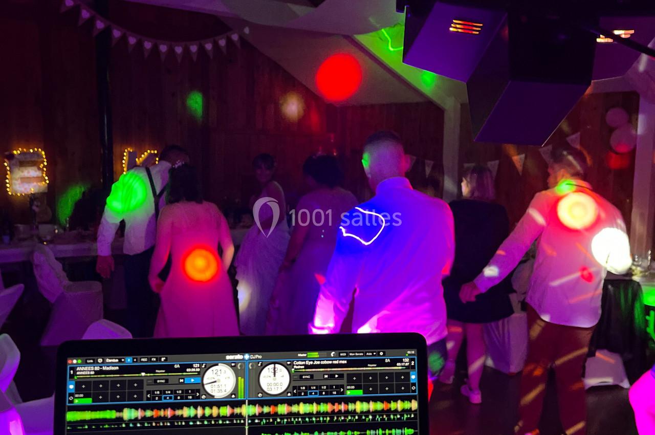 Des invités dansent sous des lumières colorées lors d'une soirée festive, avec une console DJ en premier plan.
