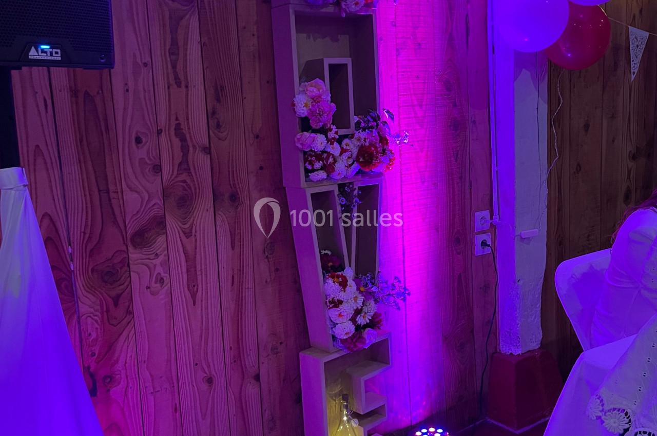 Étagère en bois formant le mot ’LOVE’, décorée de fleurs et éclairée par une lumière violette dans une salle festive.