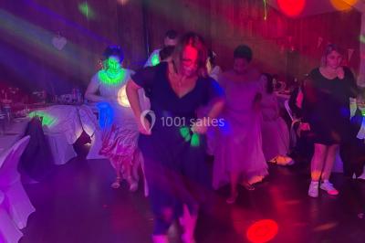 Salle en pierre avec plafond en poutres apparentes, éclairages décoratifs suspendus et équipement audio-visuel installé.