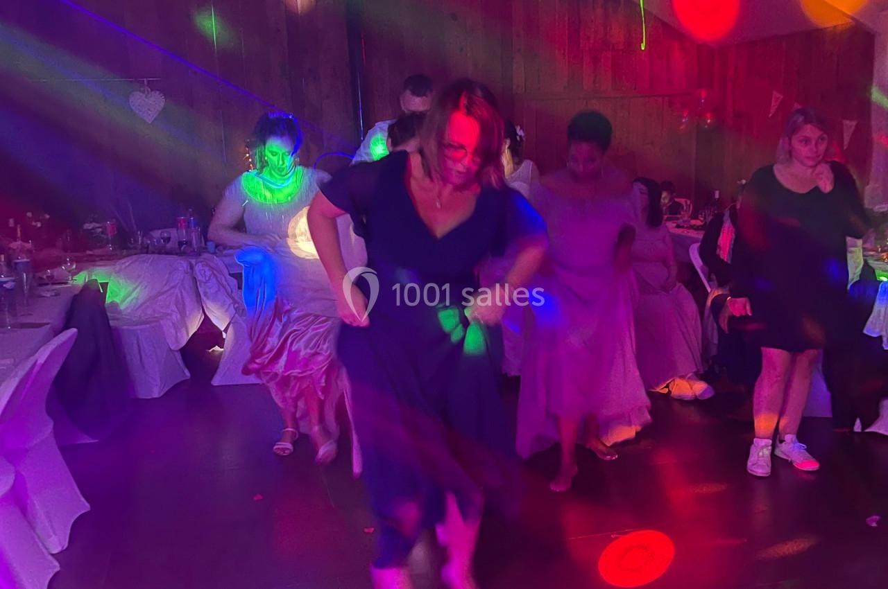 Des personnes dansent dans une salle décorée, éclairée par des lumières colorées et festives.