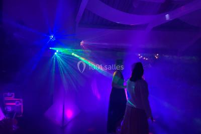 Salle en pierre avec plafond en poutres apparentes, éclairages décoratifs suspendus et équipement audio-visuel installé.