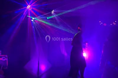 Salle en pierre avec plafond en poutres apparentes, éclairages décoratifs suspendus et équipement audio-visuel installé.