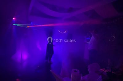 Salle en pierre avec plafond en poutres apparentes, éclairages décoratifs suspendus et équipement audio-visuel installé.