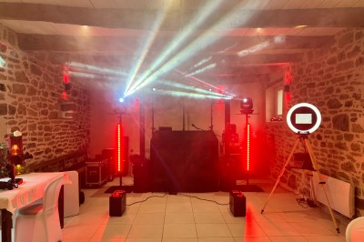 Salle en pierre avec plafond en poutres apparentes, éclairages décoratifs suspendus et équipement audio-visuel installé.