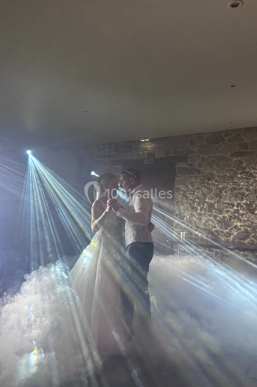 Un couple danse dans une ambiance romantique avec des faisceaux lumineux et de la fumée dans une salle en pierre.