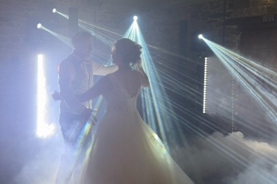 Salle en pierre avec plafond en poutres apparentes, éclairages décoratifs suspendus et équipement audio-visuel installé.