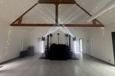 Salle en pierre avec plafond en poutres apparentes, éclairages décoratifs suspendus et équipement audio-visuel installé.