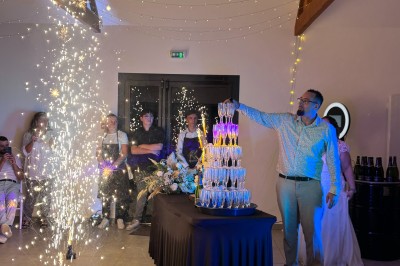 Salle en pierre avec plafond en poutres apparentes, éclairages décoratifs suspendus et équipement audio-visuel installé.