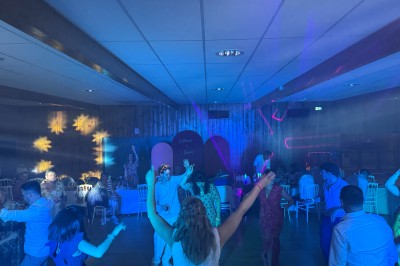 Salle en pierre avec plafond en poutres apparentes, éclairages décoratifs suspendus et équipement audio-visuel installé.