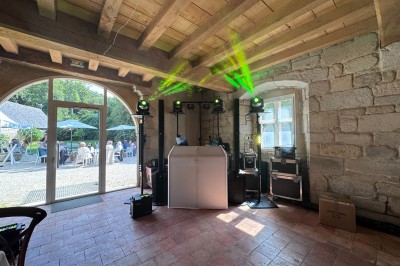 Salle en pierre avec plafond en poutres apparentes, éclairages décoratifs suspendus et équipement audio-visuel installé.