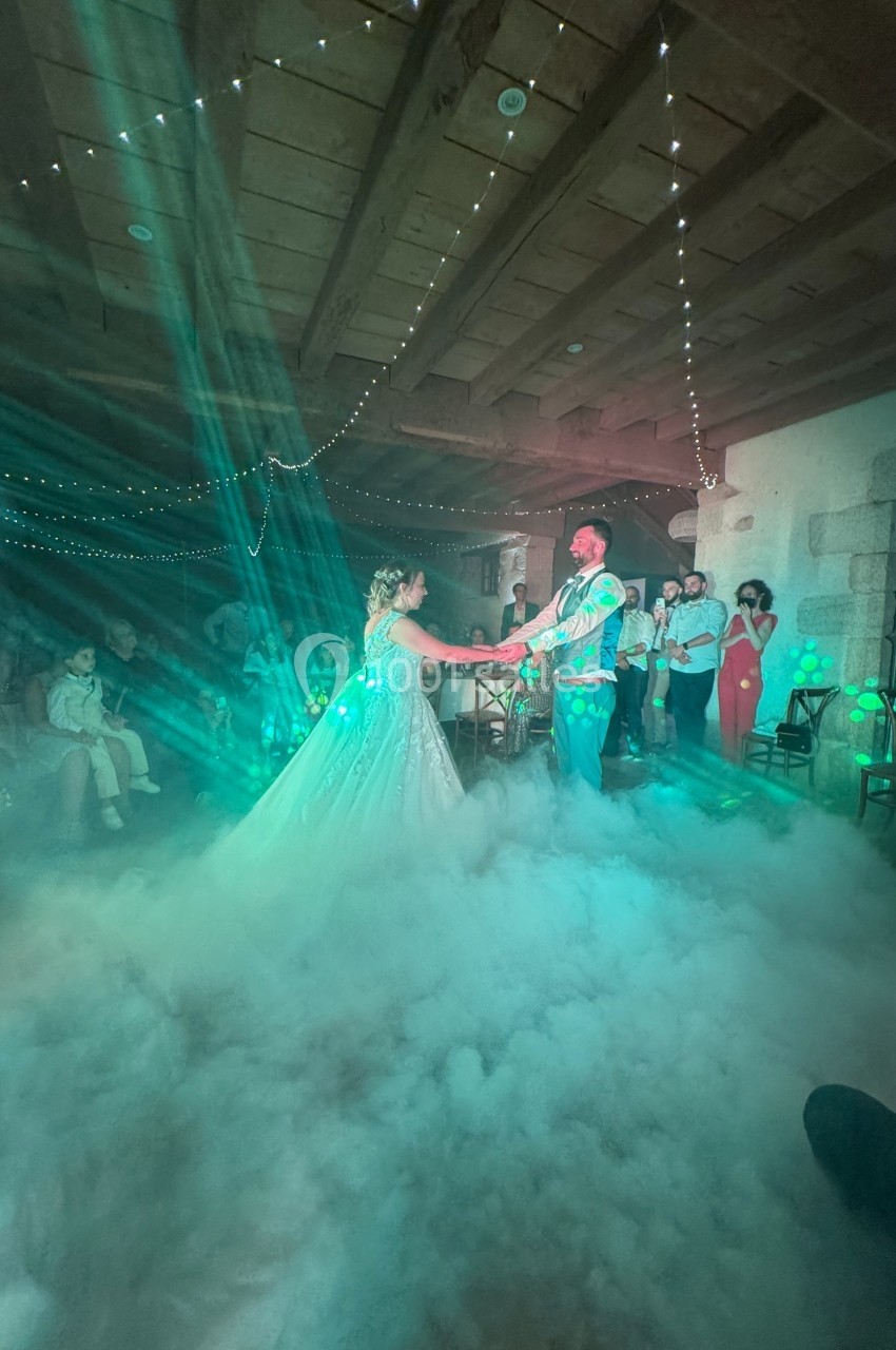 Un couple danse sous des lumières colorées et un effet de fumée dans une salle décorée de guirlandes lumineuses.