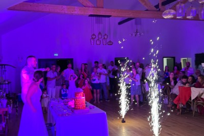 Salle en pierre avec plafond en poutres apparentes, éclairages décoratifs suspendus et équipement audio-visuel installé.