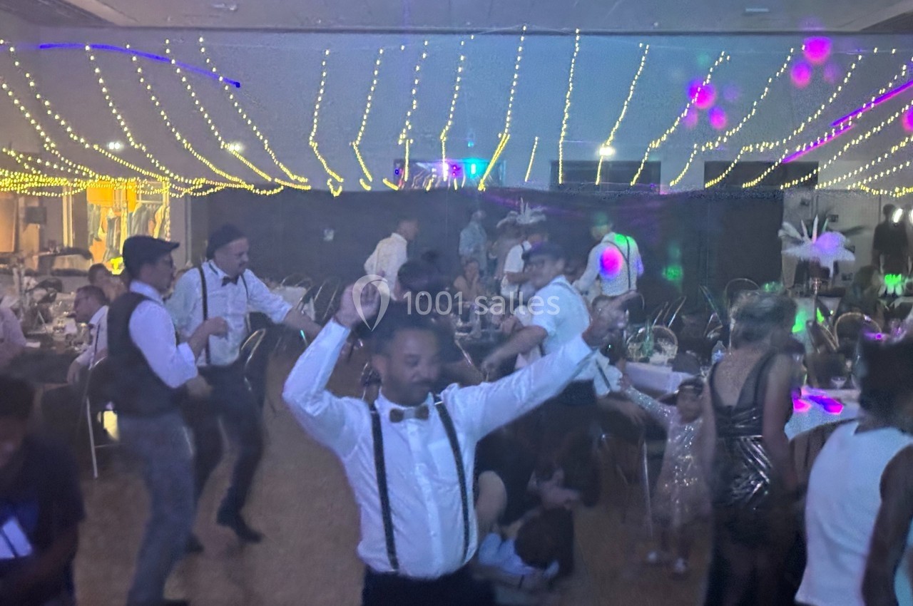 Des personnes dansent sous des guirlandes lumineuses dans une salle décorée pour une fête.