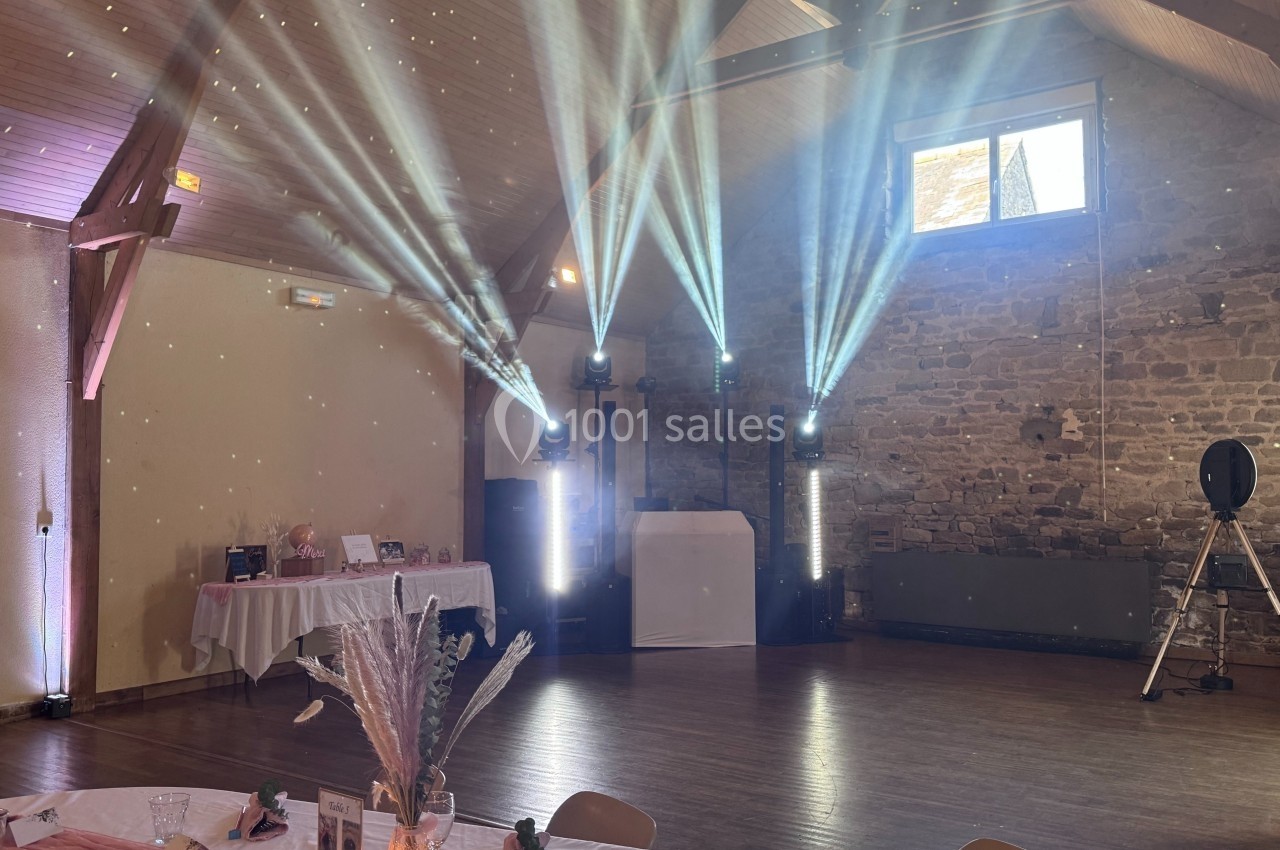 Salle de réception décorée avec des tables dressées, des faisceaux lumineux et un mur en pierre apparente.