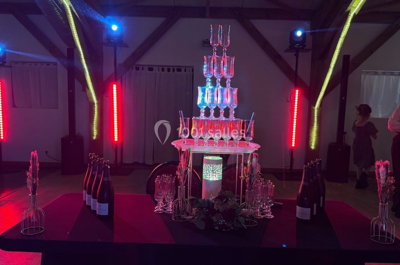 Tour de coupes en verre illuminée, entourée de bouteilles et décorations, dans une salle avec éclairage coloré.