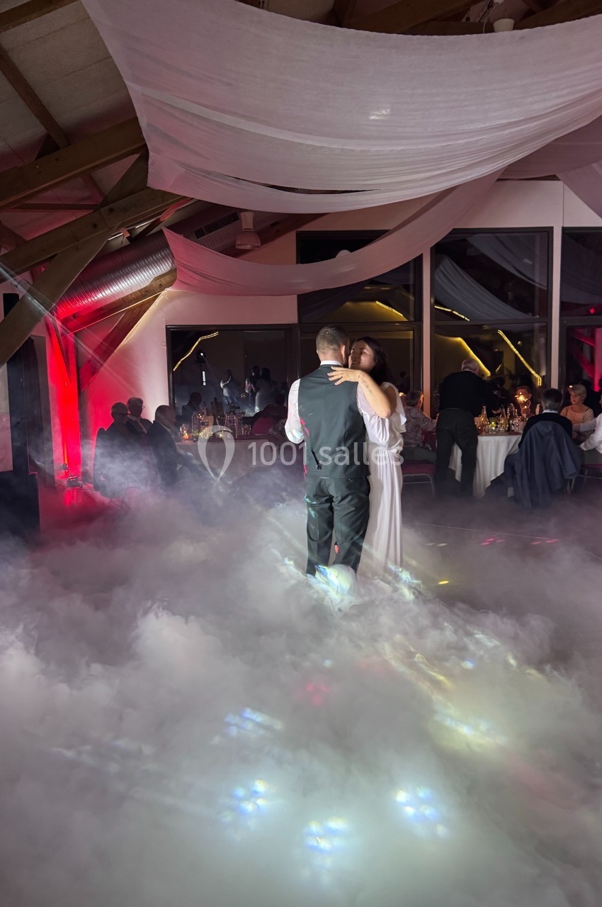 Un couple danse dans une salle décorée avec des voilages blancs et un sol recouvert de fumée légère.