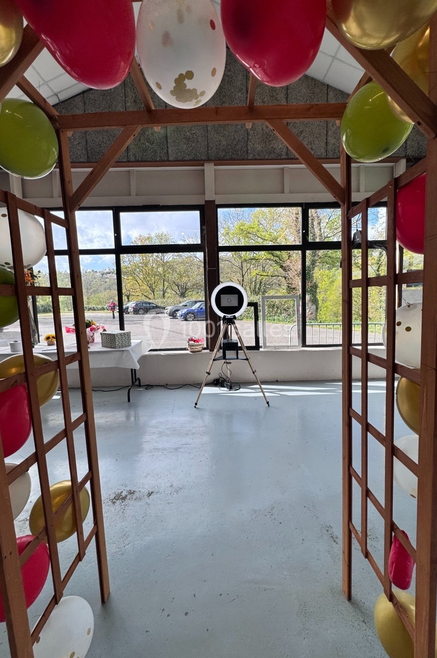 Structure en bois décorée de ballons colorés, avec un trépied et une lampe circulaire dans une pièce lumineuse.