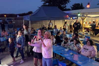 Salle en pierre avec plafond en poutres apparentes, éclairages décoratifs suspendus et équipement audio-visuel installé.