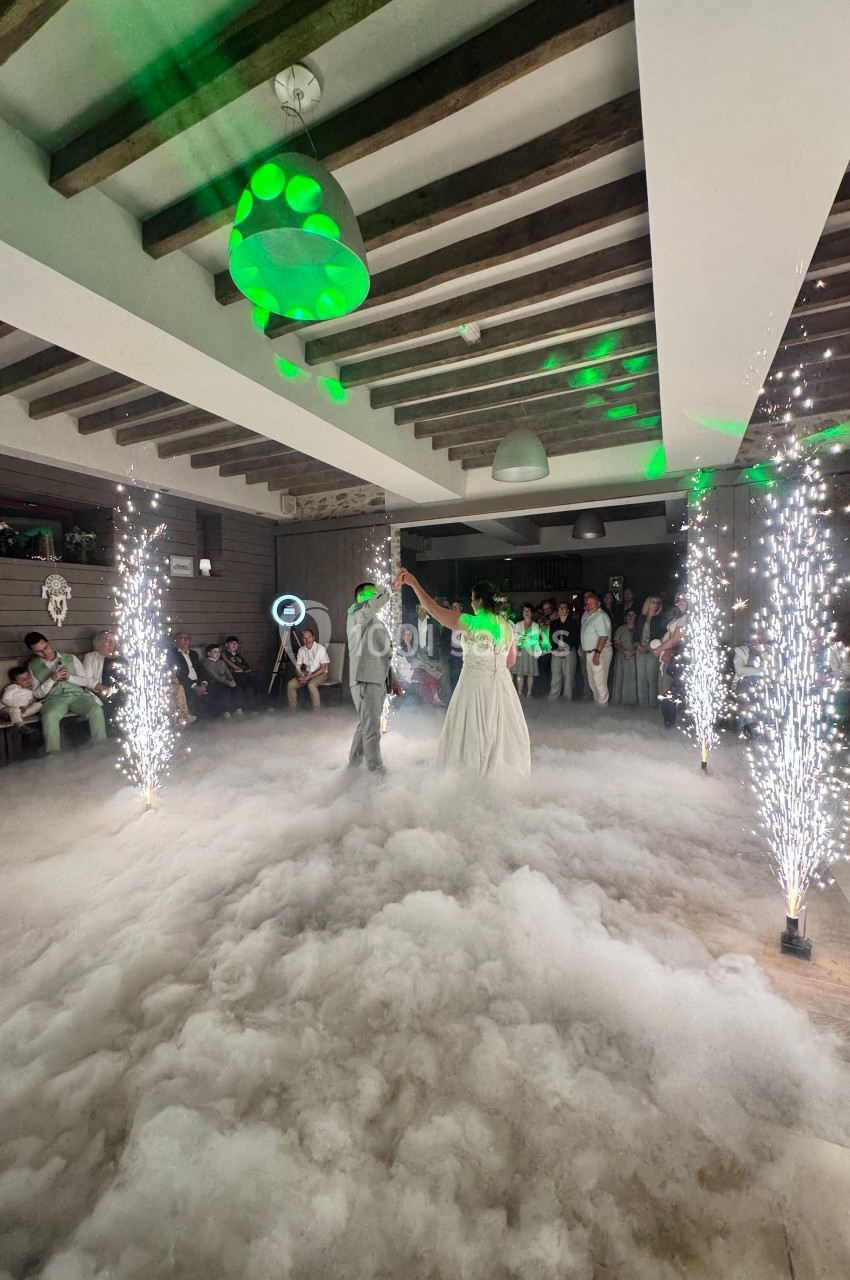 Un couple danse au milieu d'une piste enveloppée de fumée, entourée de jets d'étincelles et d'invités.